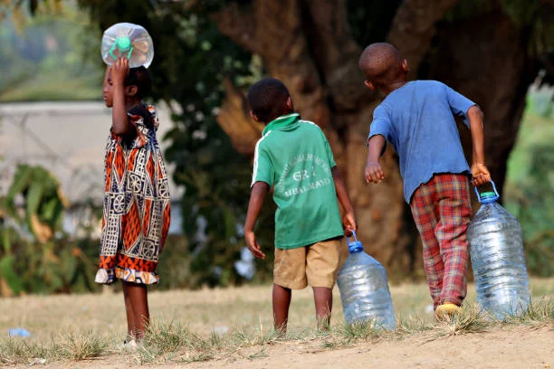 Trois enfants de dos portant des bidons d'eau